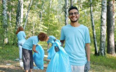 Volontärer samlar skräp i en skog med blå sopsäckar